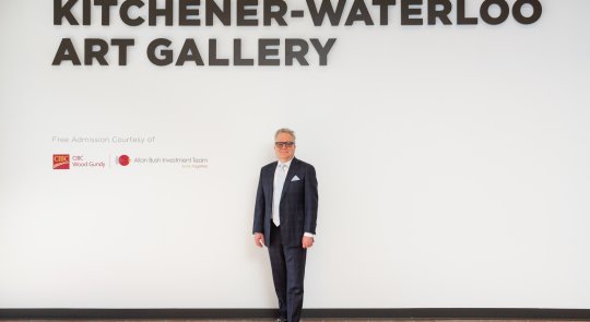 Photo of Allan Bush, an older man in a dark suit and glasses, standing alongside signage recognizing Free Admission Sponsor CIBC Wood Gundy - Allan Bush Investment Team