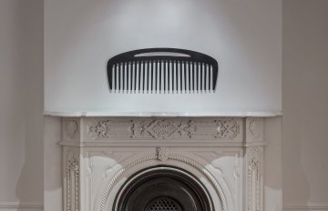 Large comb hung on a wall above a fireplace