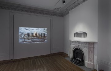 Large comb hung on a wall above a fireplace and video clip projected onto adjacent wall