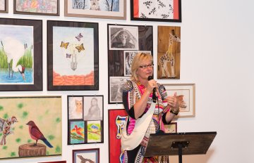 guest speaker standing in front of a wall of artwork talking about students who participated in the exhibition