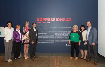 hosts and guests of exhibition opening standing in front of exhibition description and signage