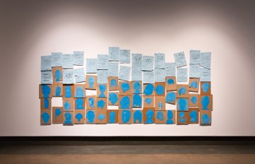 many pieces of blue paper with artwork on them hung on the gallery wall
