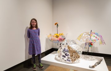 girl standing beside a sculpture on the floor of the art gallery