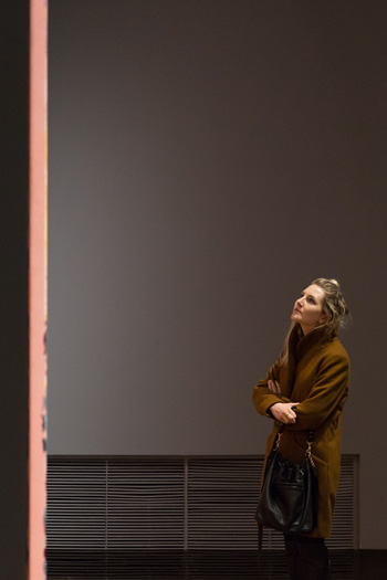 A woman gazes up at a large painting, unseen except for the edge of its canvas, in a darkened gallery at KWAG