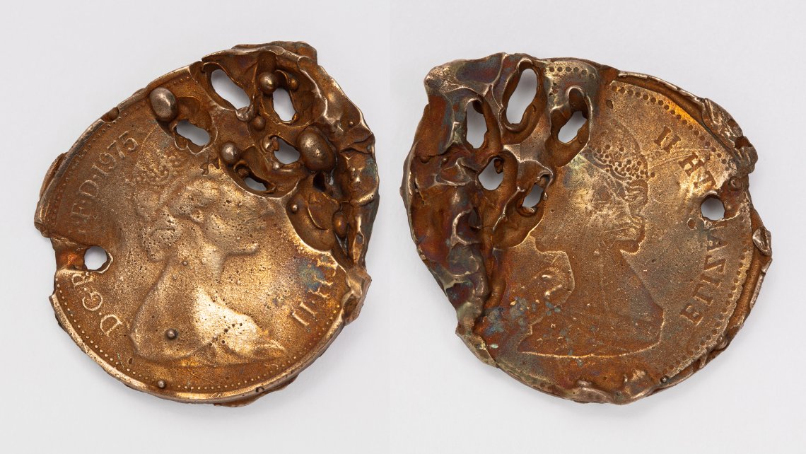 Photograph of two altered pennies with drill holes running through them. They are on a white background.