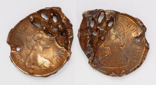 Photograph of two altered pennies with drill holes running through them. They are on a white background.
