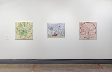 Three of Greg Curnoe's watercolor paintings of a bicycle wheel on a green background, a Mariposa bicycle and another bicycle wheel painting with a red background