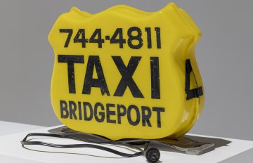 Photo of an antique yellow, plastic Taxi sign for the top of a car