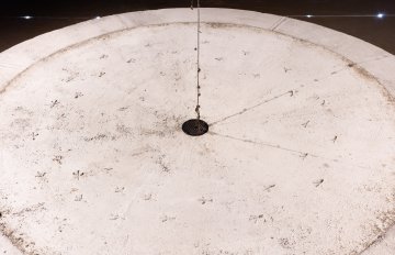 View from above of the concrete structure similar to a foundatin. A drain hole is clearly dark and has a small metal cover on it