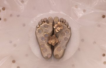 View of a casting of feet from underneath in gold on a background of concerete, interspersed with coins.