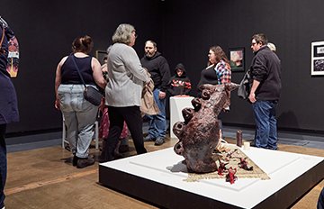 Group of people walking around a selection of art hung on walls and a sculpture on the gallery floor