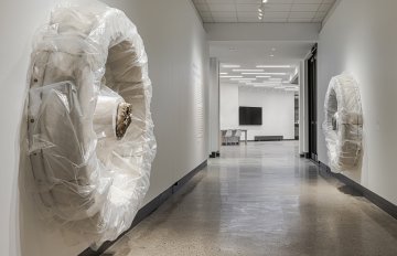 Concrete sculpture wrapped in plastic with a casting of feet emerging from the centre