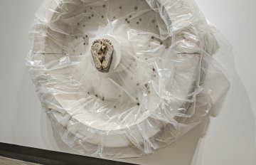 Concrete sculpture wrapped in plastic with a casting of feet emerging from the centre