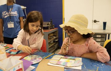 Two campers sitting together looking at each other's artwork