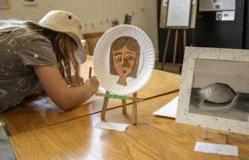 Student propping up a clay-based portrait on an easel