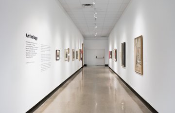 View down the middle of a corridor with a grey floor, a white wall on each side has artwork hung on it