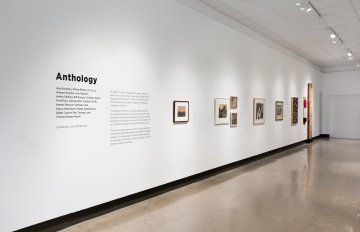 View down the middle of a corridor with a grey floor, a white wall on each side has artwork hung on it