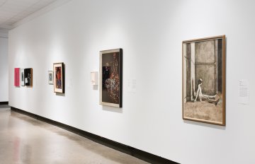 View down the middle of a corridor with a grey floor, a white wall on each side has artwork hung on it