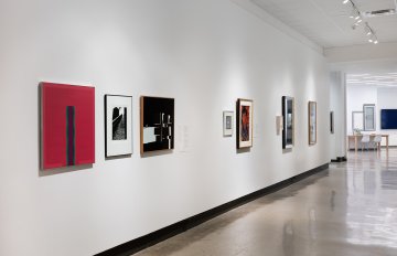 View down the middle of a corridor with a grey floor, a white wall on each side has artwork hung on it