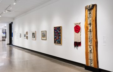 View down the middle of a corridor with a grey floor, a white wall on each side has artwork hung on it