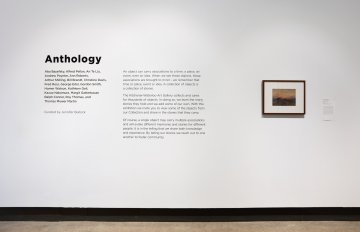 Photo of the black didactic text explaining the Anthology exhibition concept, one framed artwork is mounted on the wal beside it