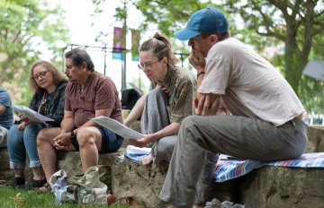 Photo from below of four people holding reading material sitting on rocks in a garden