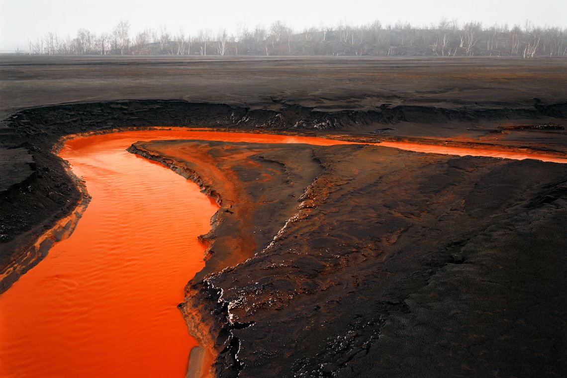 Aerial photo of vivid red nickel tailings in a river bed curling around barren-looking land