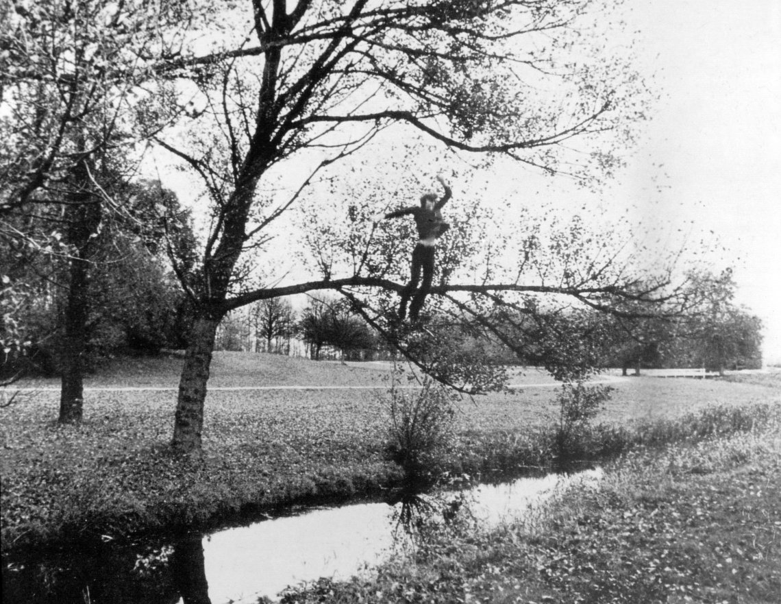 A video still from 16mm film of a man on a tree branch about to fall into a stream