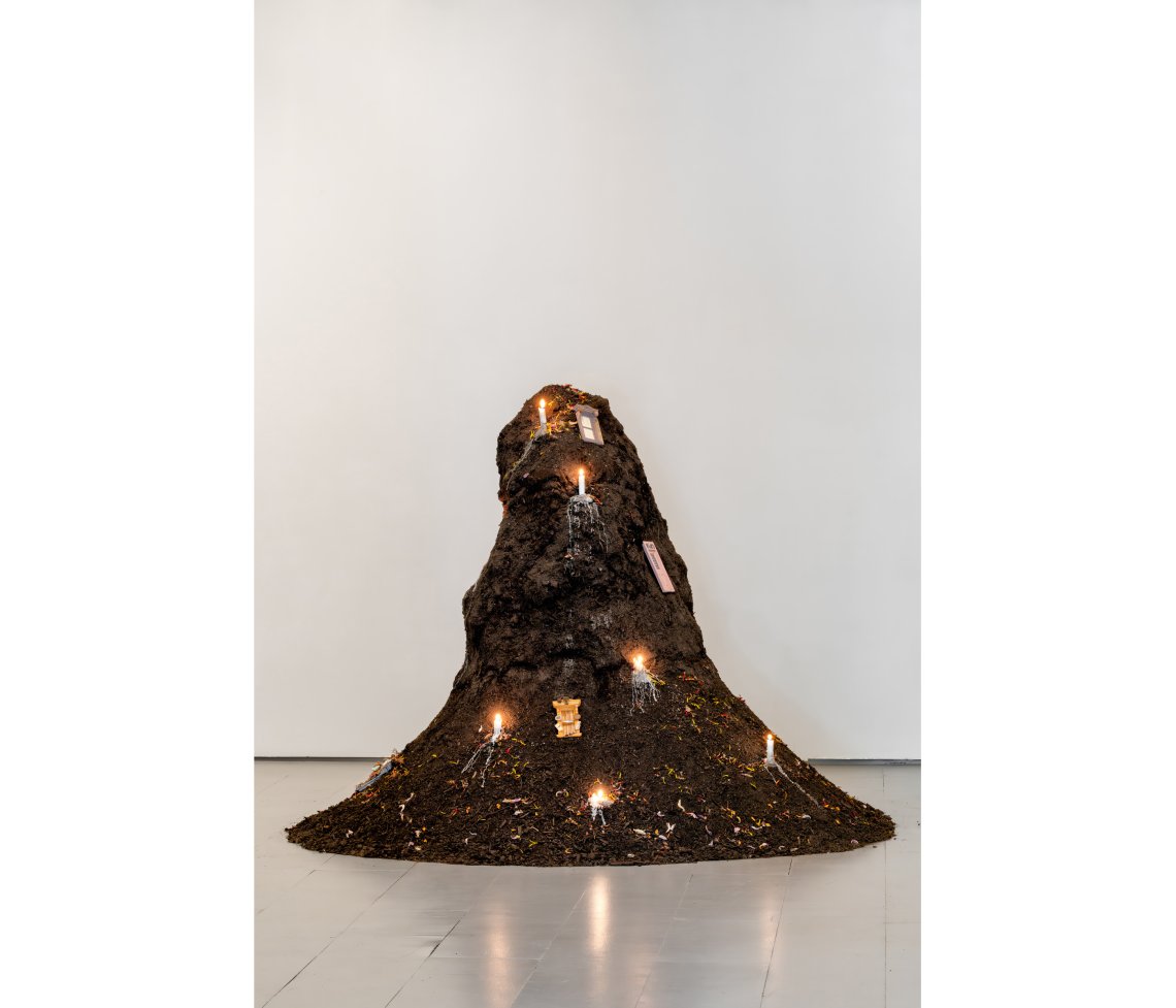 Mound of soil with lit candles spread throughout with a small fairy door on the top side
