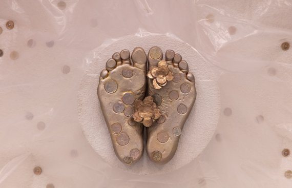 View of a casting of feet from underneath in gold on a background of concerete, interspersed with coins.