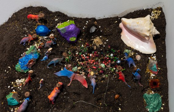 Mound of soil with colorful plastic dinosaurs and a seashell spread throughout with a small fairy door on the top side
